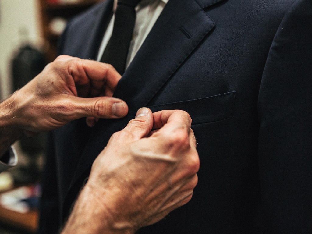 A tailor's hands adjusting the lapel of a dark jacket